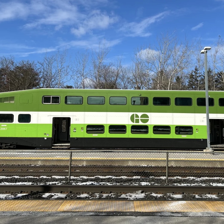 A bright green commuter train in motion beside a snowy platform, representing the powerful rumble and whoosh of a moving train.