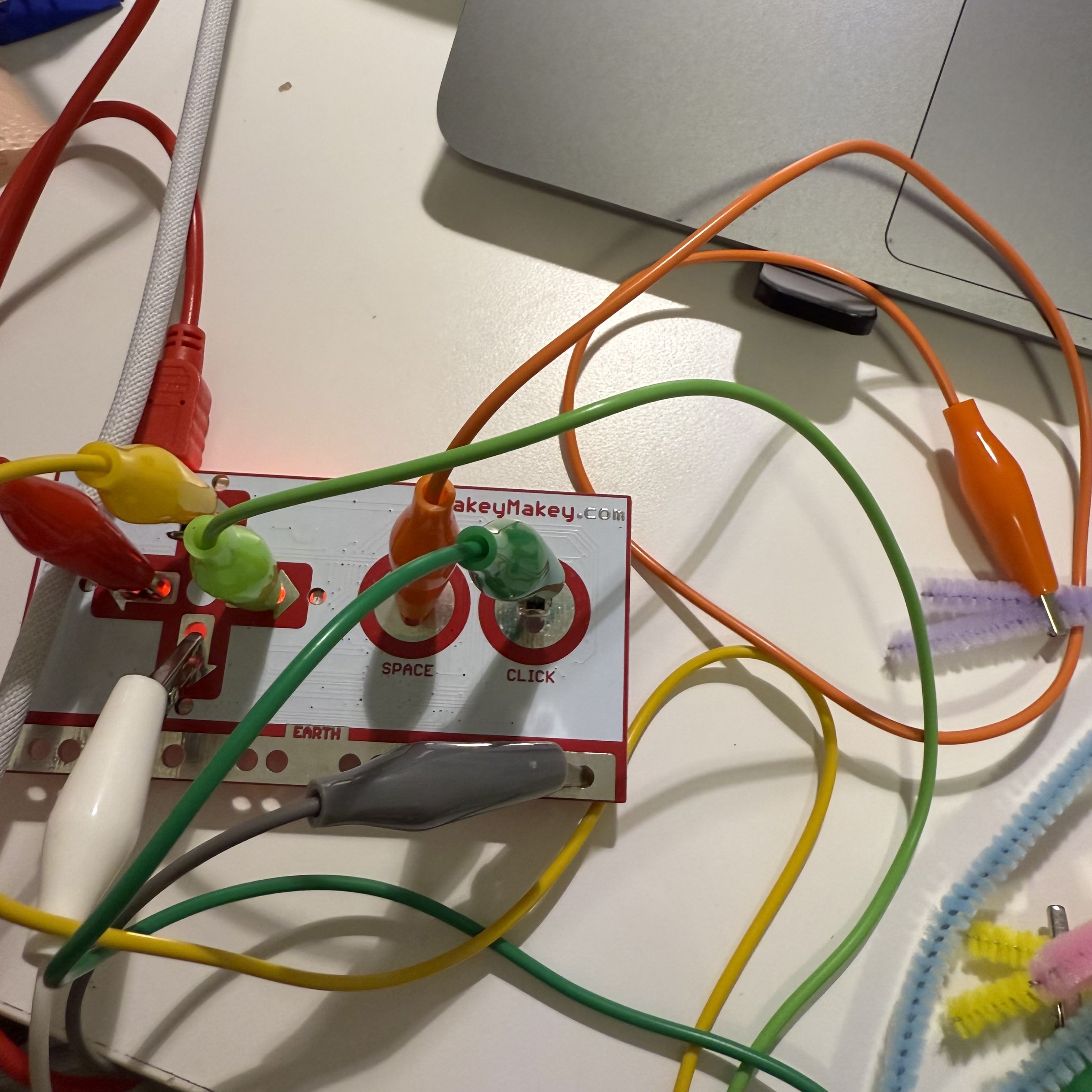 The Makey Makey board is visible here, showing various wires connected to the colorful pipe cleaners. This setup allows me to experiment with different interactive projects, combining creativity and technology to make unique digital interactions.