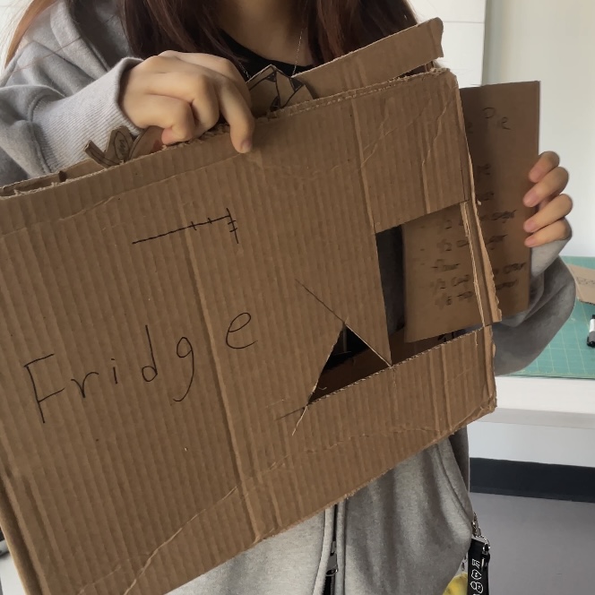 <b>Smart fridge</b><br>This cardboard box represents our smart fridge. When the user opens it, the fridge shows the apple pie recipe and expiry alerts. It is used to communicate suggestions and guide the next steps.